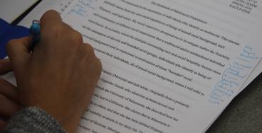 Hand with blue pen giving written feedback on student paper