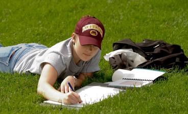 Student laying in grass and writing
