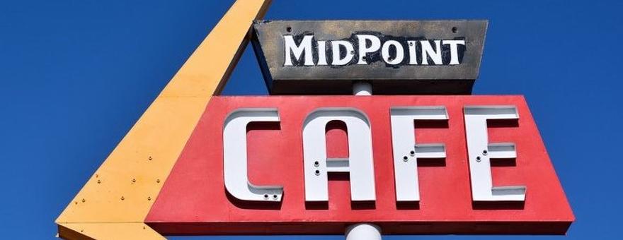 Top of road sign for MidPoint Cafe with blue sky background