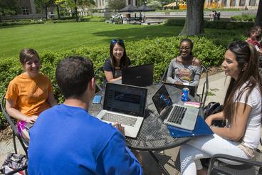 Students sitting with laptop on outdoor table on campus.