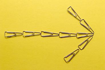 Paper clips arranged to form an arrow with a yellow background.